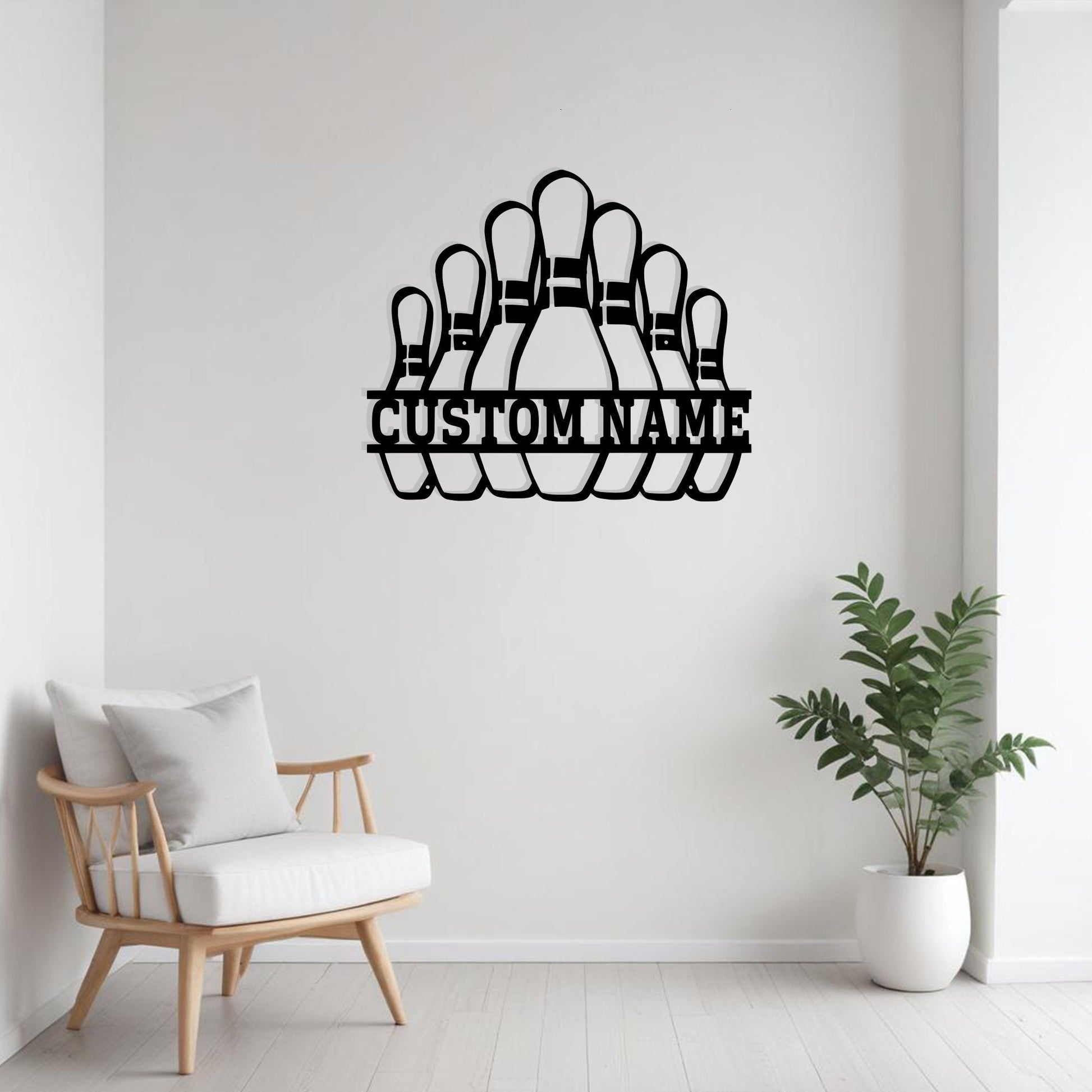 Black metal bowling pins wall art with “Custom Name” cutout above a white armchair with orange accent pillows, decorative side table, and indoor greenery