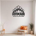 Black metal bowling pins wall art with “Custom Name” cutout above a white upholstered chair and small potted plant against a light gray wall
